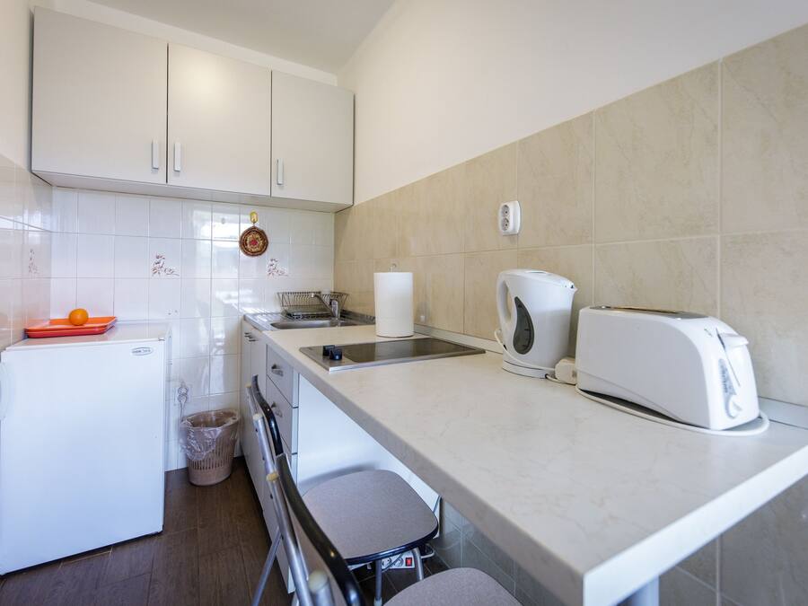 A compact kitchen with white cabinets, a small refrigerator, a toaster, and a kettle.