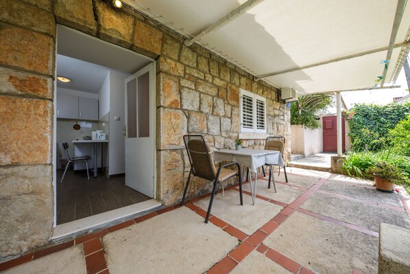 A stone exterior with a covered patio, a dining area with chairs, and a kitchen visible through an open doorway. - Guesthouse Anica (Dubrovnik)
