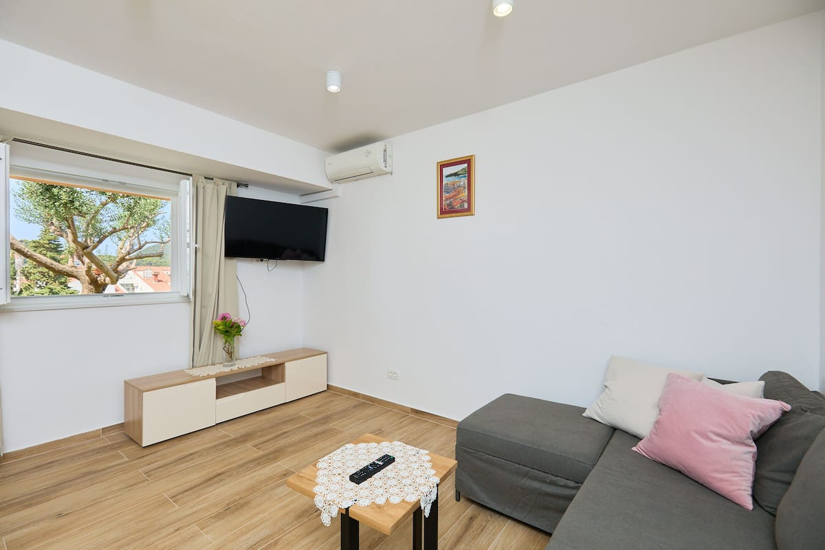 Uma sala de estar moderna com sofá, uma mesinha, televisão na parede e janela com cortinas.