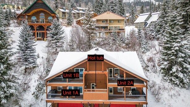 A multi-story lodge with a hot tub, labeled as Unit 1B, and two other units, Unit 1A and Unit 2A, surrounded by snow-covered trees and other buildings. - Ski in Ski out, well appointed 4 bed, 4 bath, with hot tub and lake views! (Sandpoint)