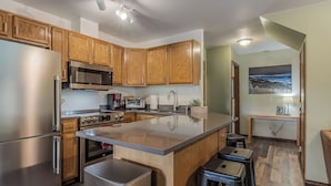 A modern kitchen with wooden cabinets, stainless steel appliances, and a large island with stools. - Ski in Ski out, well appointed 4 bed, 4 bath, with hot tub and lake views! (Sandpoint)