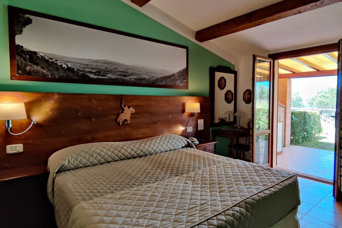 Ein Schlafzimmer mit Bett, Nachttischlampen, einem Holzkopfstück, einem Wandbild und Blick ins Freie.