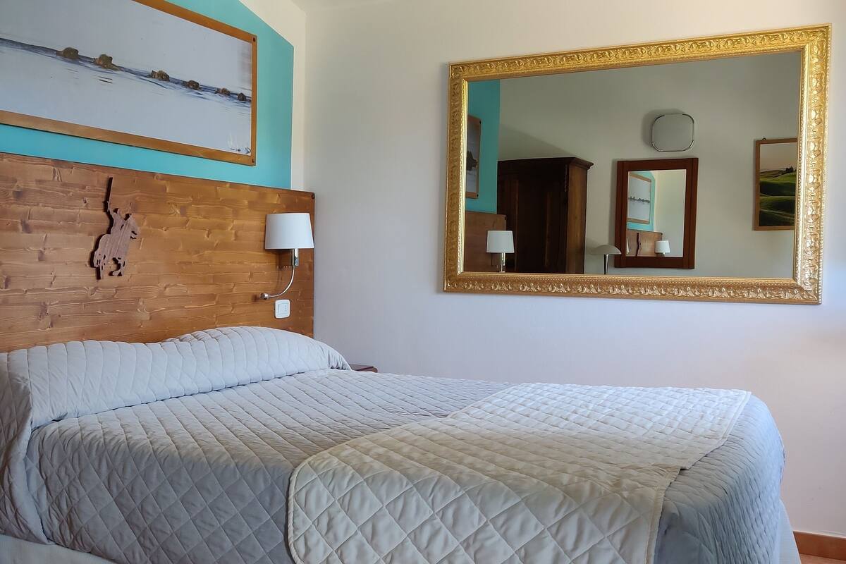 Ein Hotelzimmer mit einem hölzernen Kopfteil, einem großen Bett mit gesteppter Bettdecke, zwei Nachttischlampen, einem Nachttisch mit Telefon und einem gerahmten Bild über dem Bett.