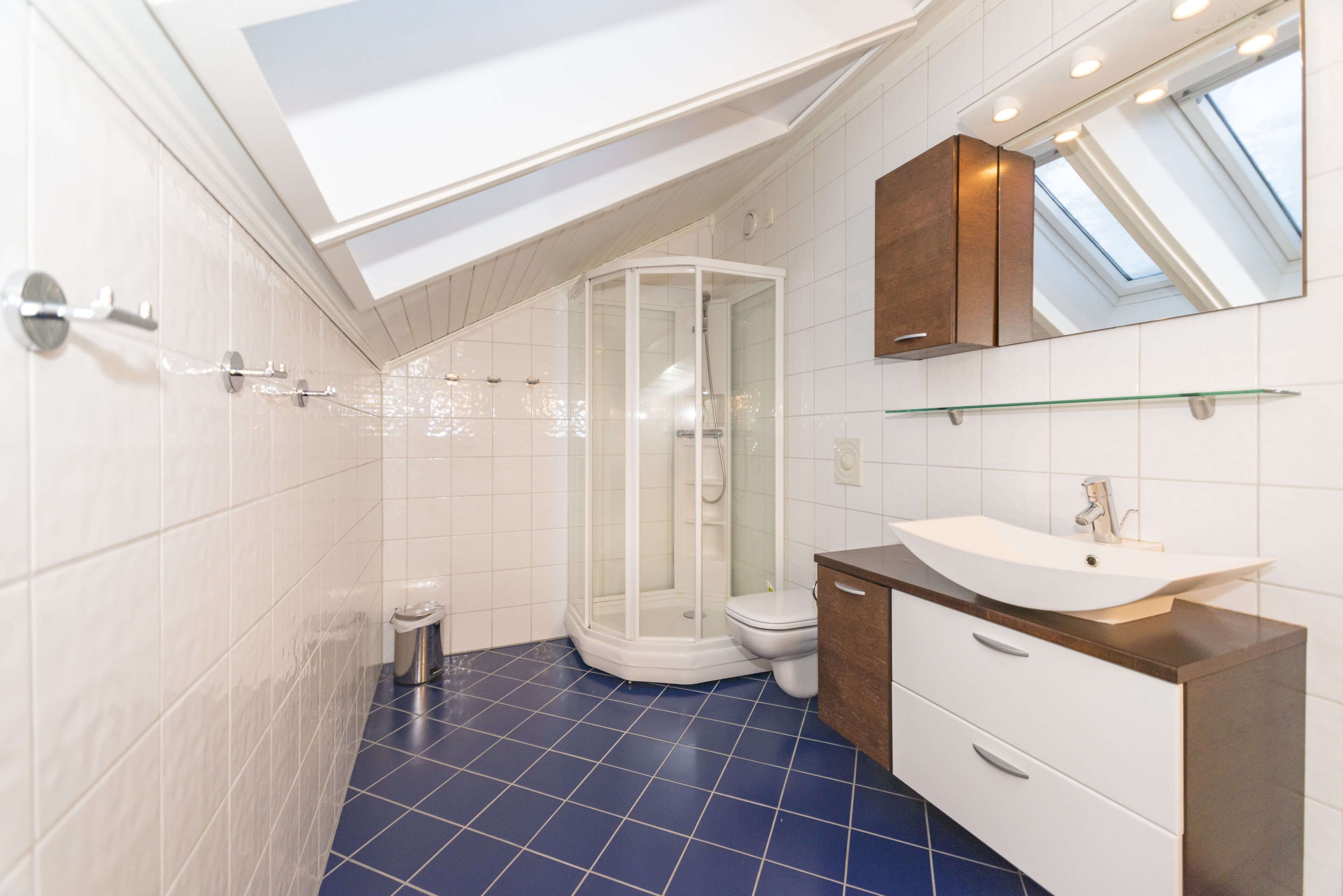 Un baño moderno con tragaluz, cabina de ducha de vidrio, lavabo blanco y tocador de madera.