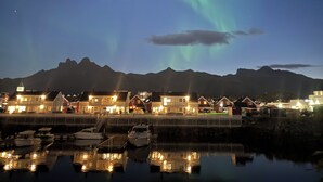 A waterfront view with boats docked, a row of houses with lights, and a mountain range in the background. - Rorbuene Svolvær Havn (Vagan)