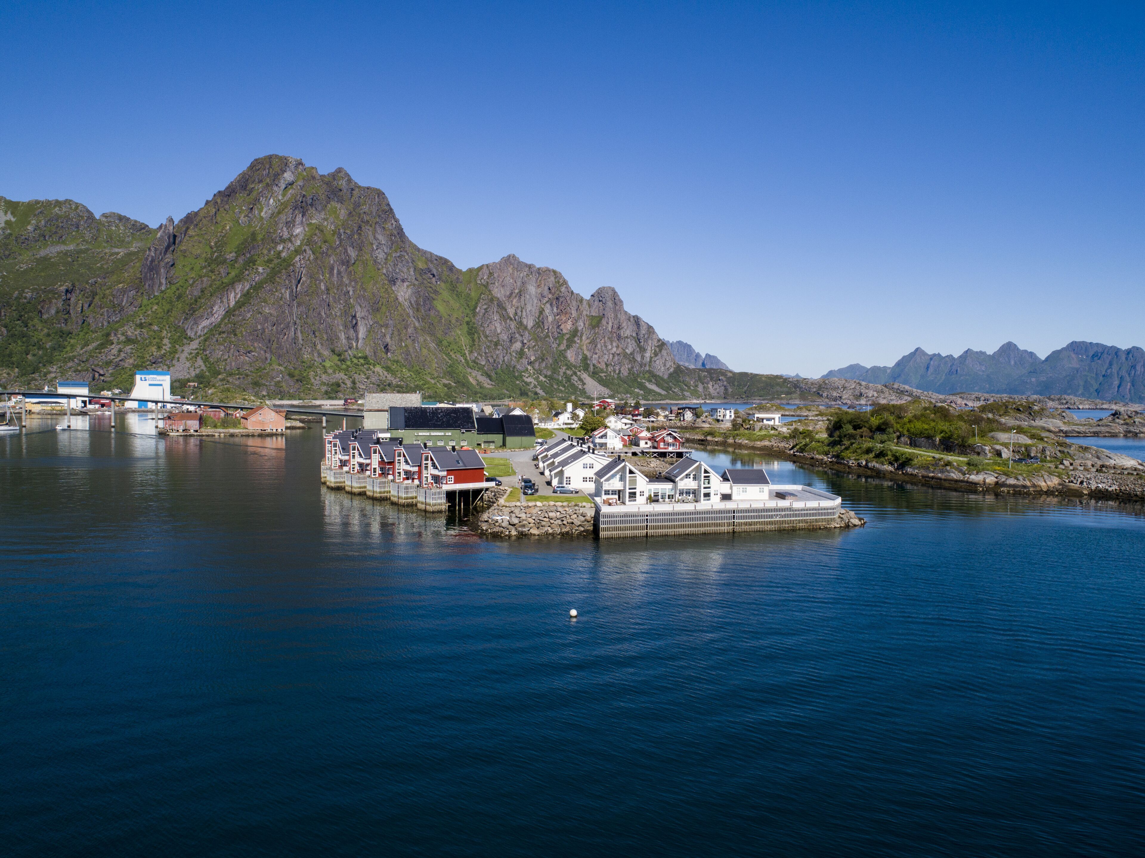 A coastal town with a dock, buildings, and mountains in the background.