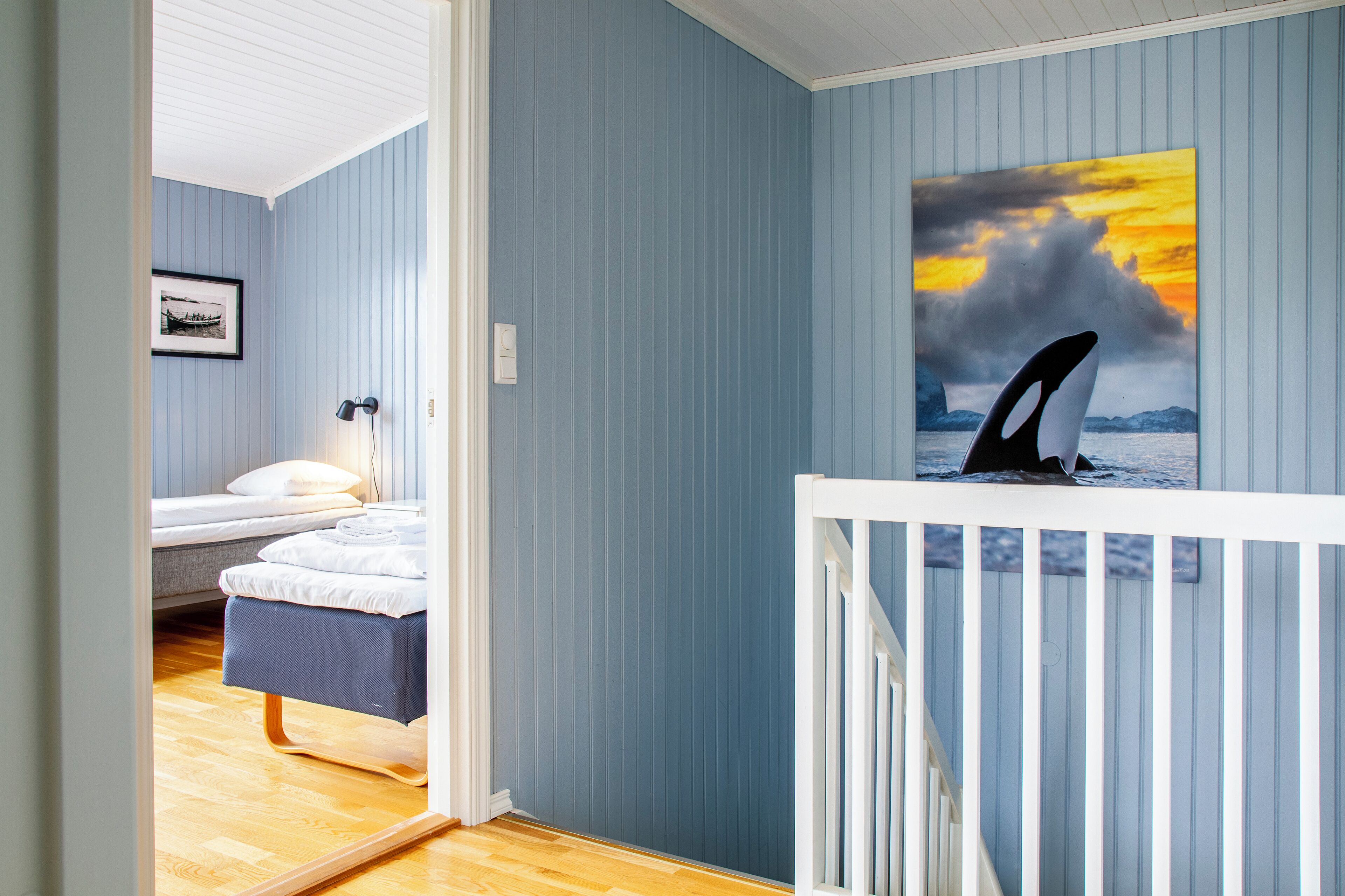 A room with a bed, a bedside table, a framed picture on the wall, and a large painting of an orca.