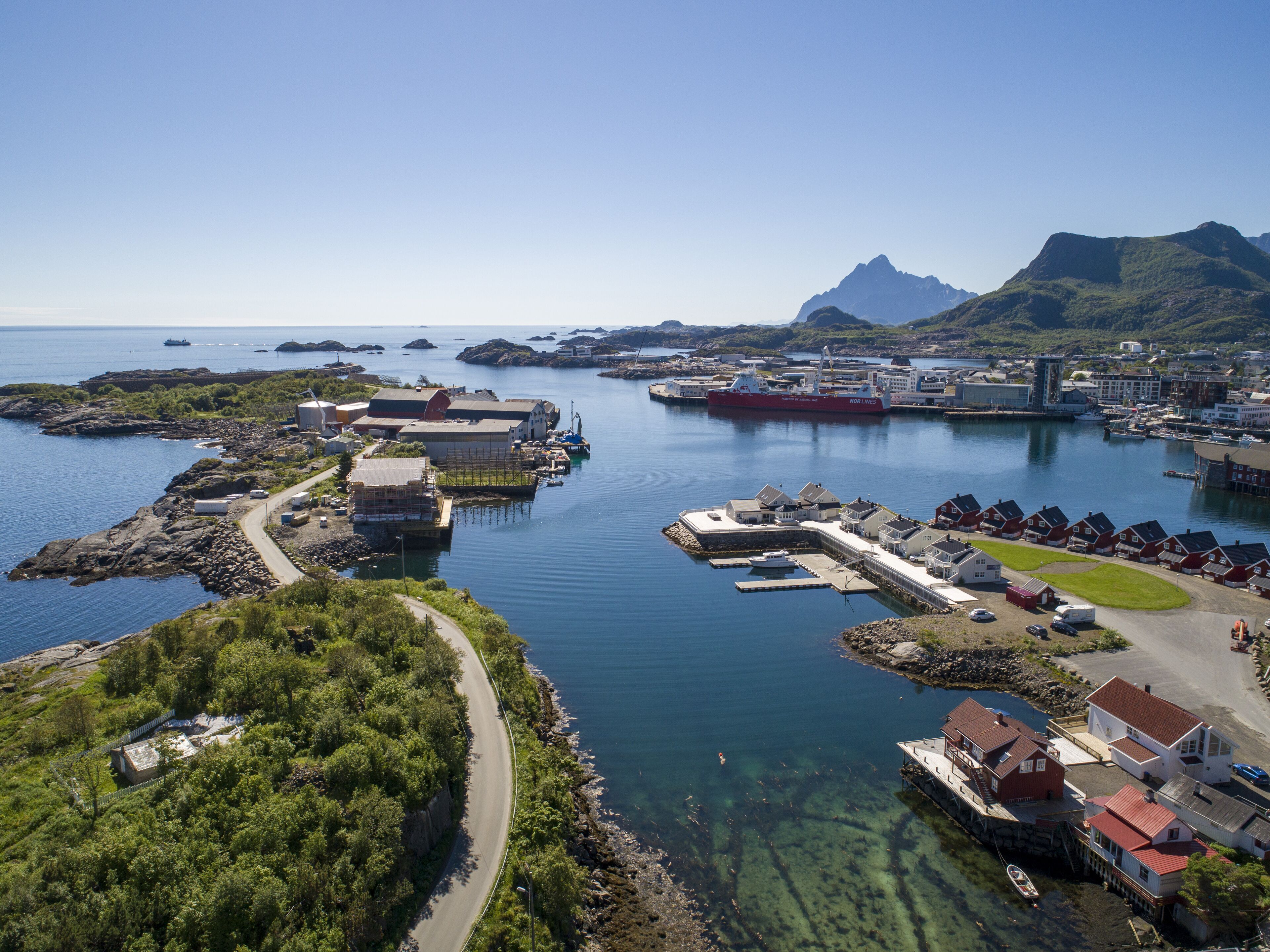 A coastal town with a marina, houses, and a prominent mountain in the background.