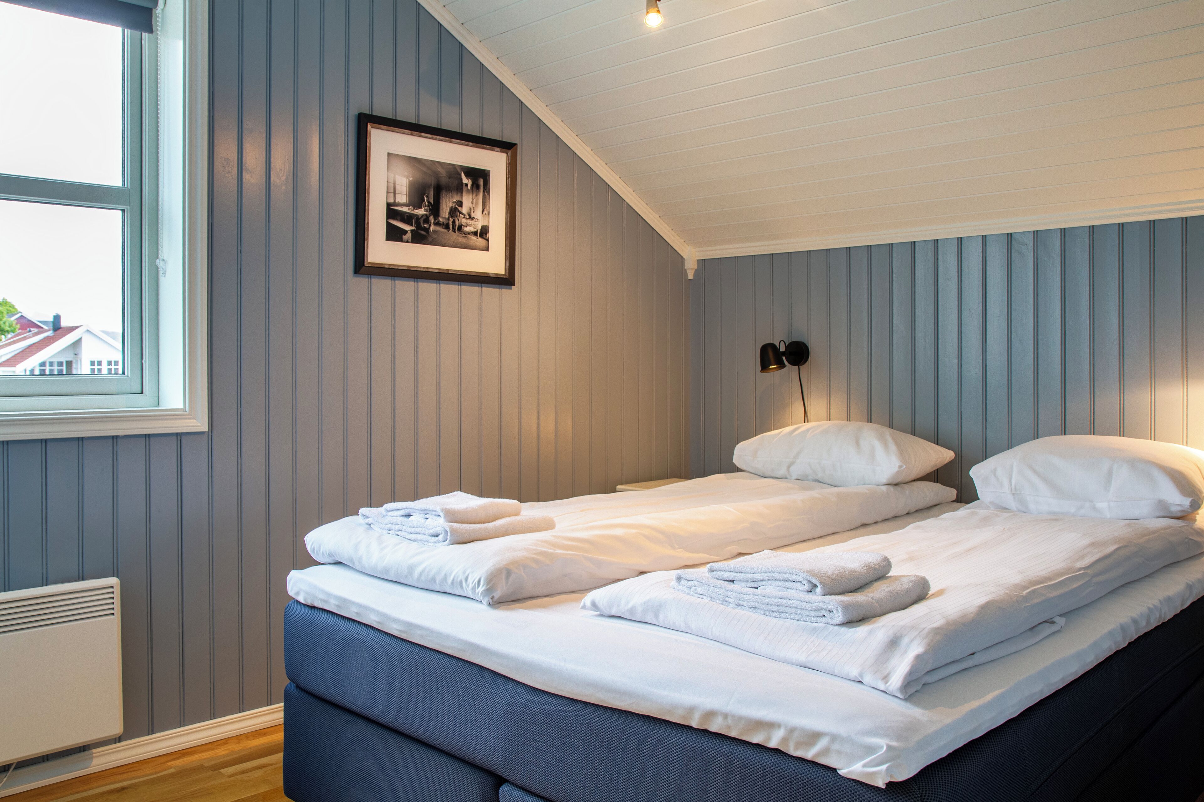 A bedroom with two beds, a framed photo on the wall, and a window with a view of buildings.