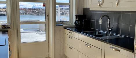 Una cocina con suelo de madera, armarios blancos, encimera negra y vistas a un paisaje rocoso a través de las ventanas.