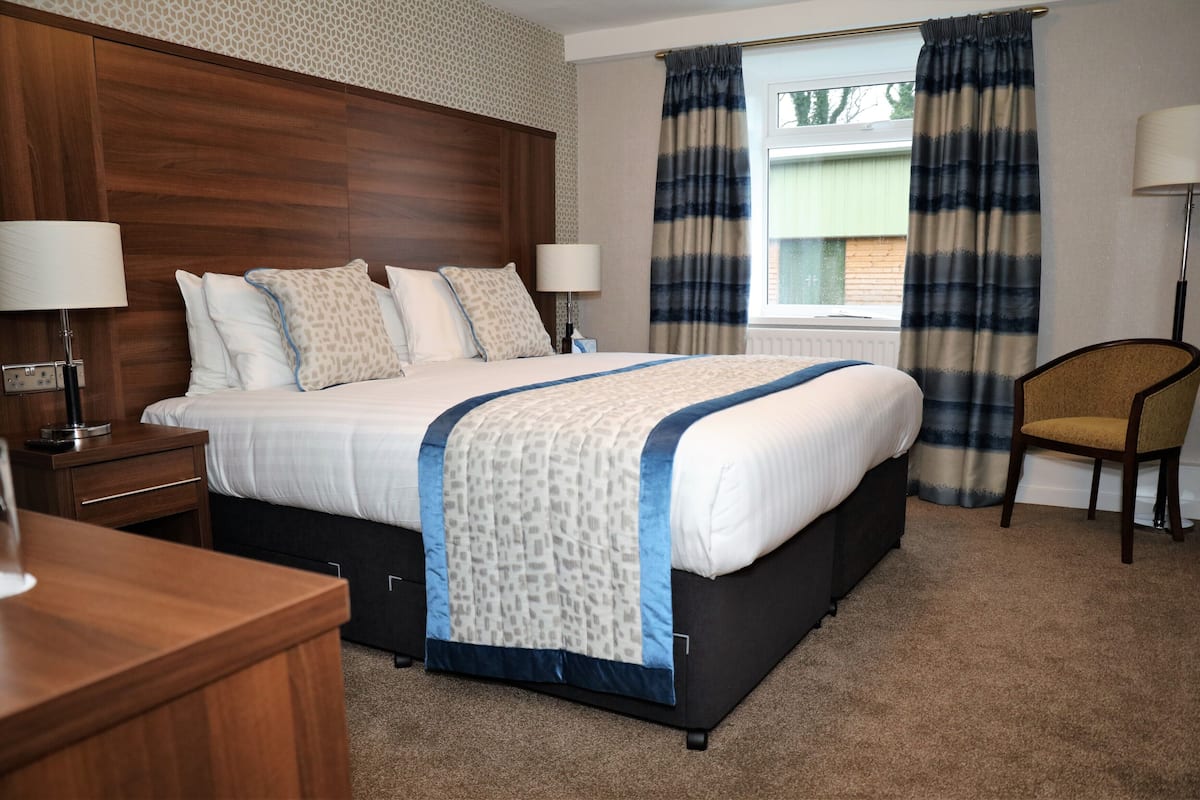 Habitación de hotel con una cama grande, dos mesitas de noche con lámparas, una silla y una ventana con cortinas.