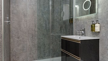 A modern bathroom with a glass shower enclosure, a white sink, a dark vanity, and a large mirror.