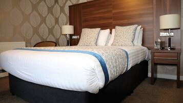 Habitación de hotel con una cama grande, un cabecero de madera, dos mesitas de noche con lámparas y un papel tapiz estampado.