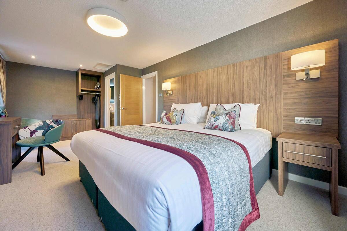 Una habitación de hotel moderna con una cama grande, mesitas de noche, una silla y un armario.