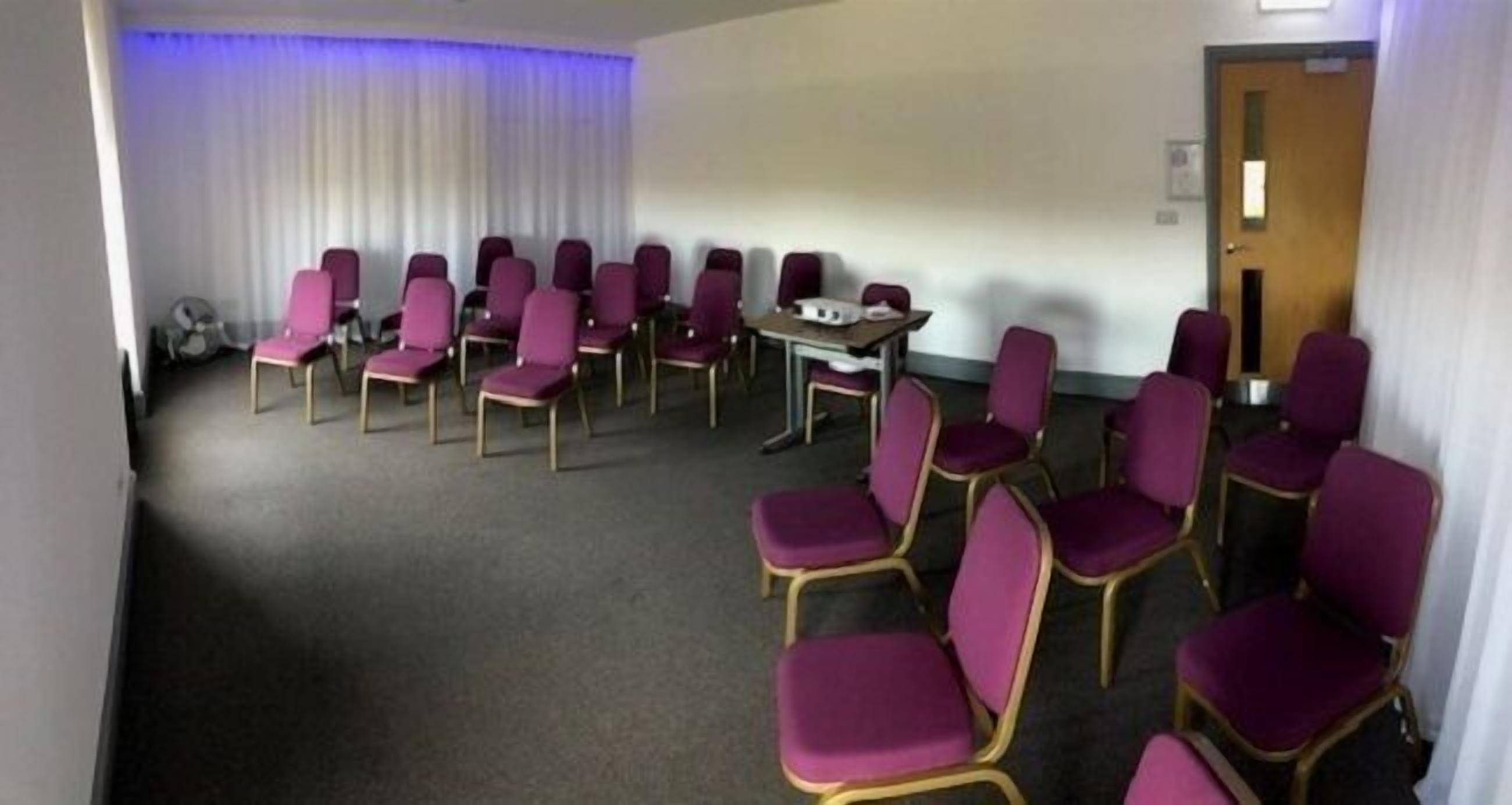 Una sala de conferències amb files de cadires morades, una taula i una pissarra.