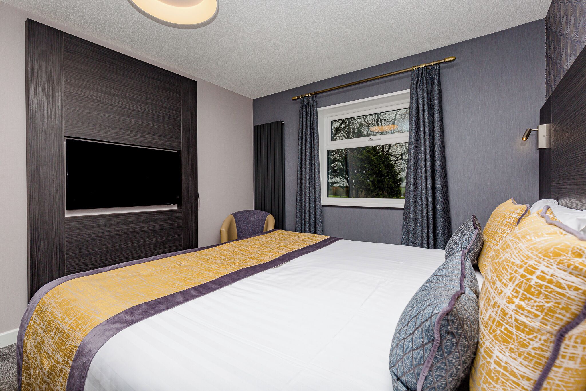 A hotel room with a large bed, a flat-screen TV, a window with curtains, and a chair.
