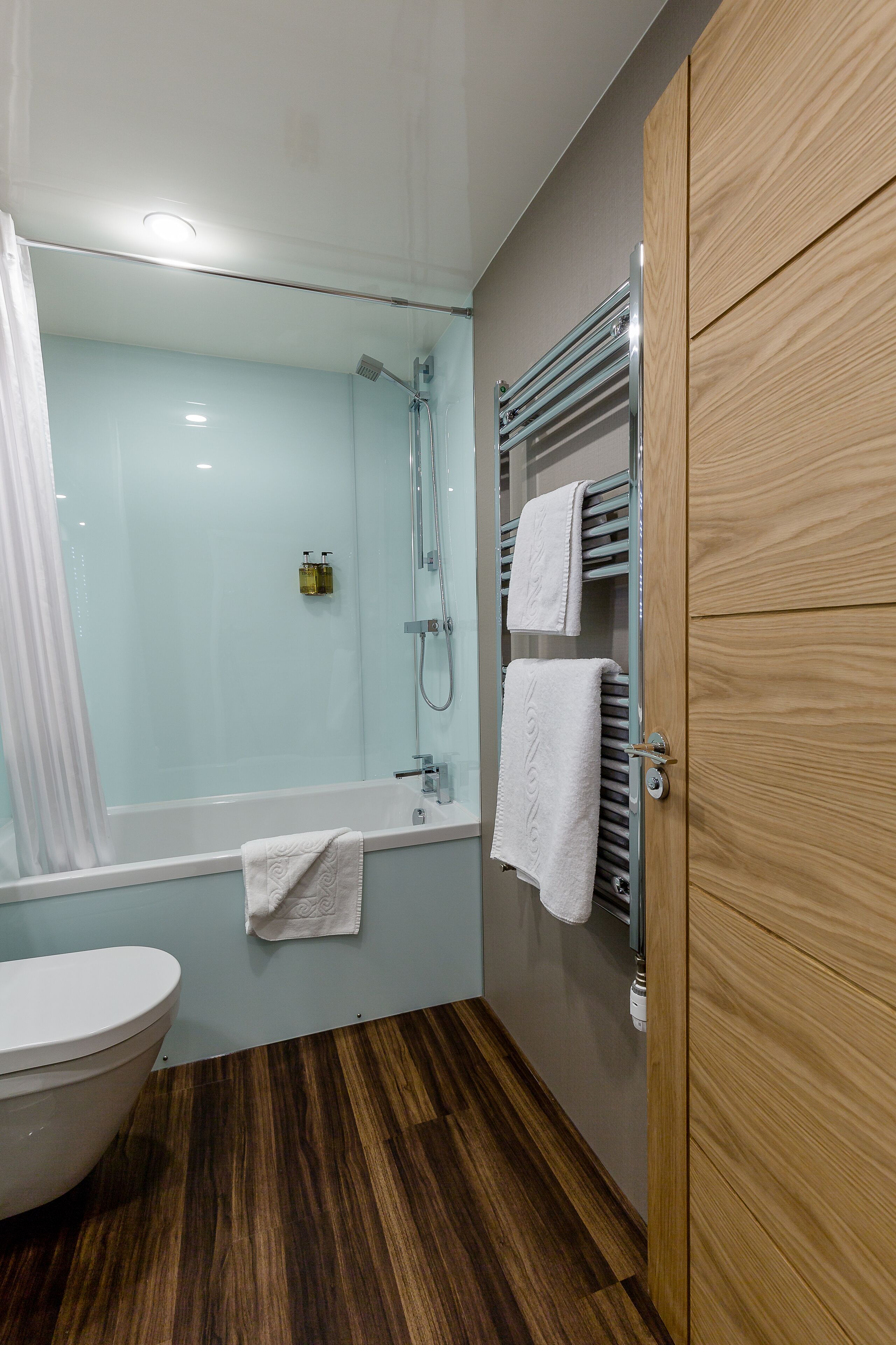 A modern bathroom with a glass-enclosed shower, a wooden vanity, and a white toilet.