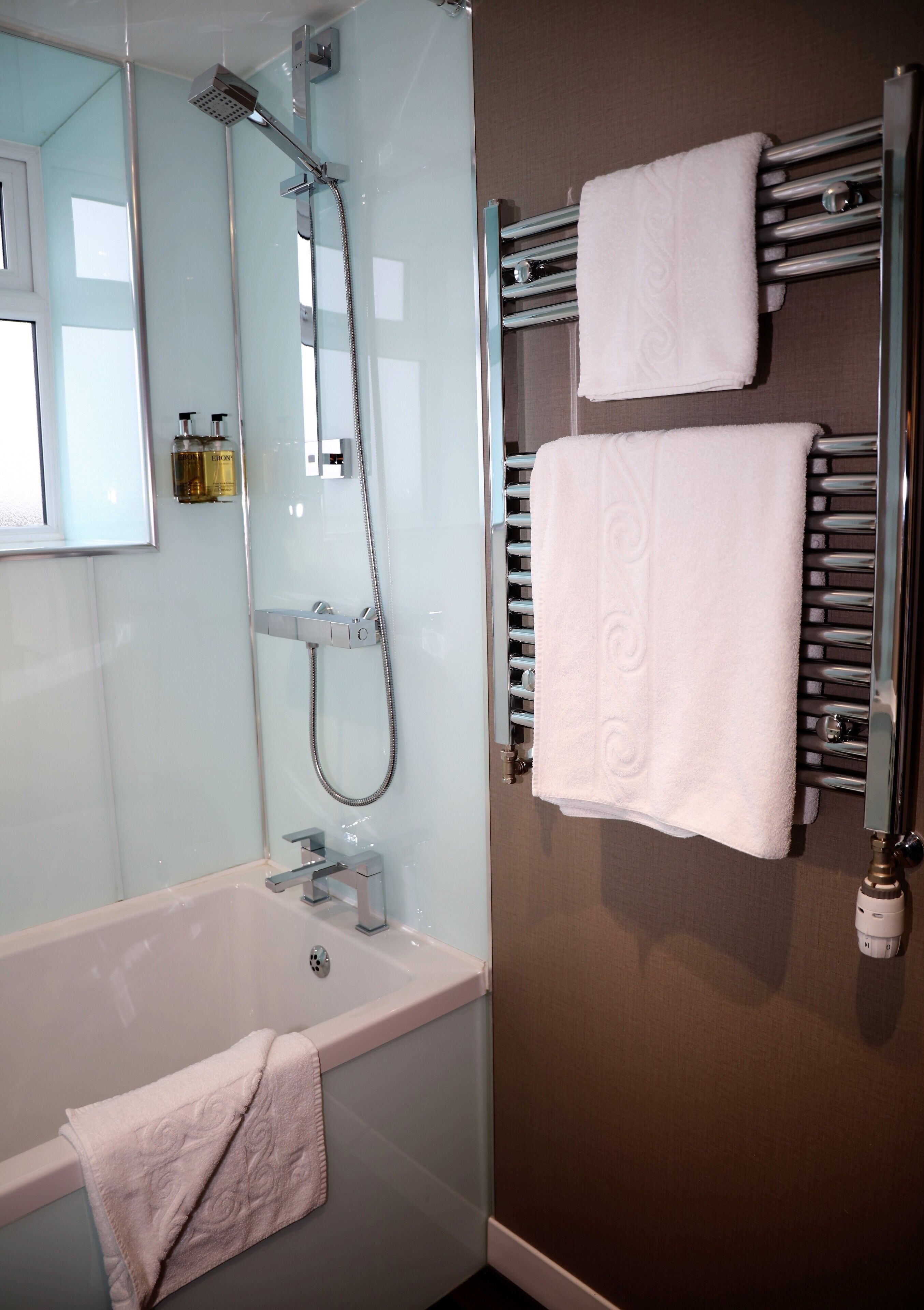 A modern bathroom with a bathtub, a glass-enclosed shower, and a towel rack with two towels.