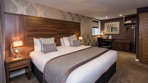 A hotel room with a large bed, a desk, a chair, a vanity with a mirror, and a wardrobe. - The Melbreak Hotel (Workington)