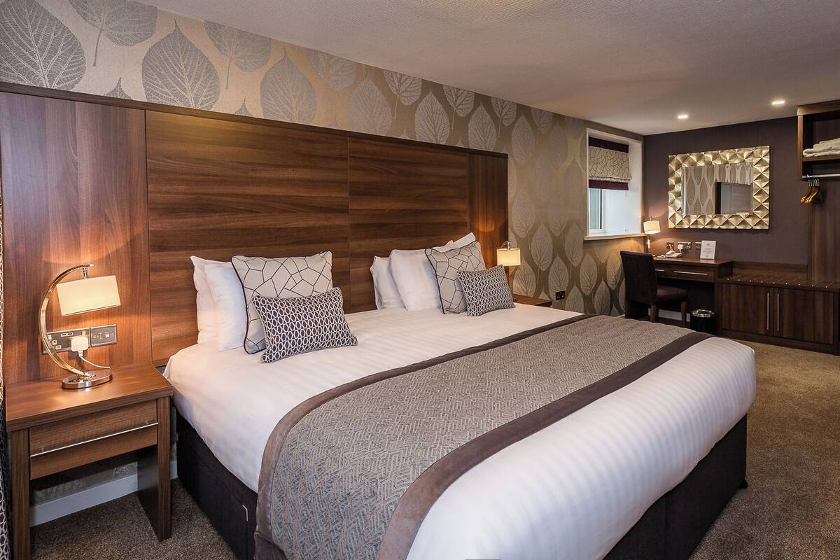 Habitación de hotel con una cama grande, un escritorio, una silla, tocador con espejo y armario.