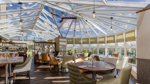 A spacious restaurant with a high ceiling and large windows, featuring wooden flooring and modern furniture. - The Melbreak Hotel (Workington)