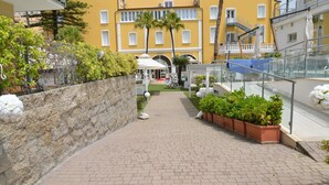 A paved pathway leading to a building with a yellow facade, a palm tree, and outdoor seating. - Mediterraneo Palace Depandance (Amantea)