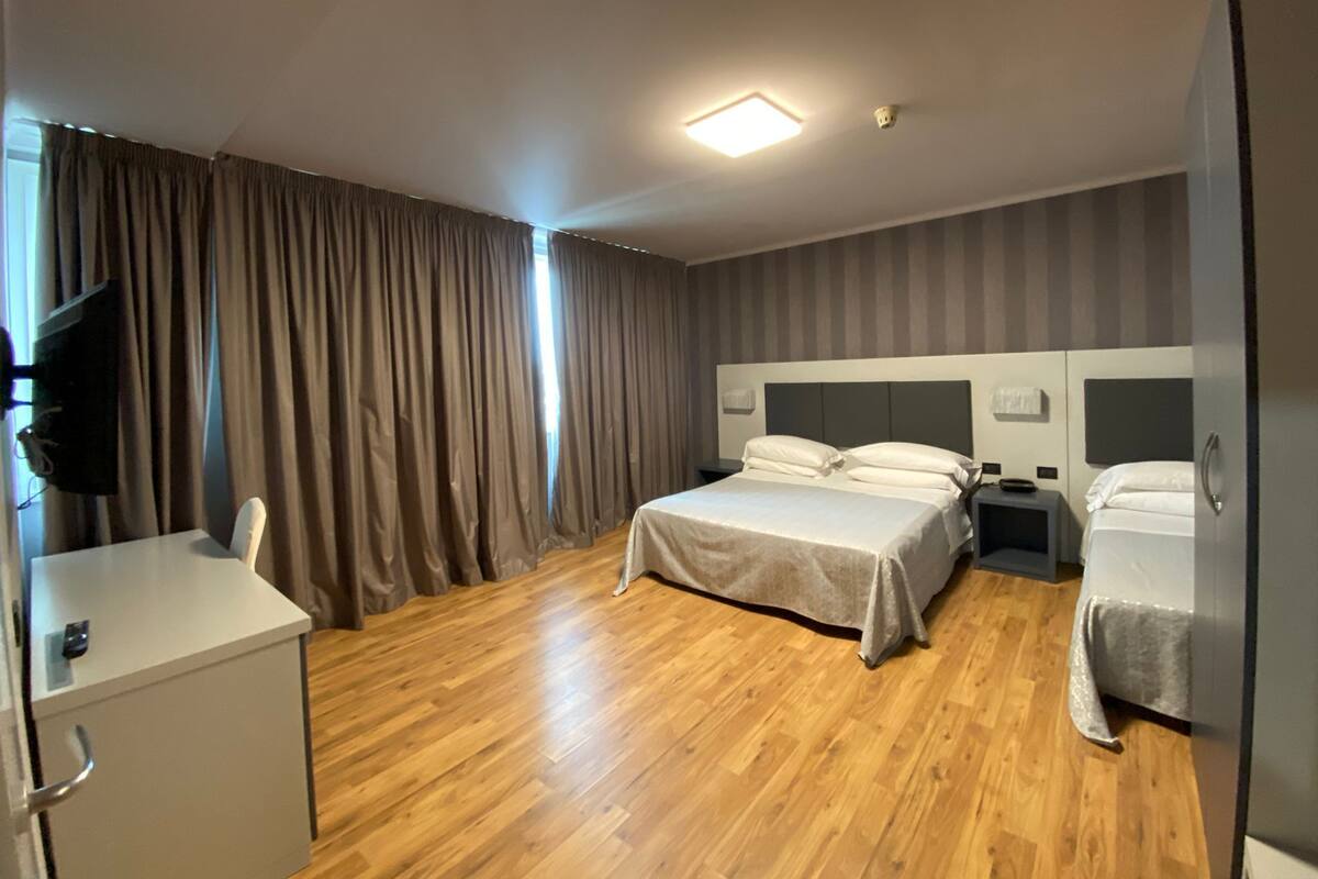 Una habitación de hotel con cama, escritorio, silla, televisor y armario.