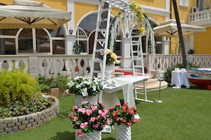 Un espace patio extérieur avec une table blanche, une chaise blanche et une arche blanche décorée de fleurs.