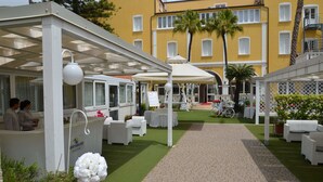A courtyard with outdoor seating, a reception desk, and a building in the background. - Mediterraneo Palace Depandance (Amantea)