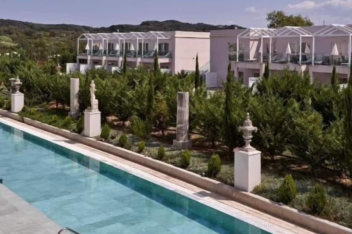 Vista de la piscina de un resort con varias villas blancas, cada una con un espacio exterior cubierto.