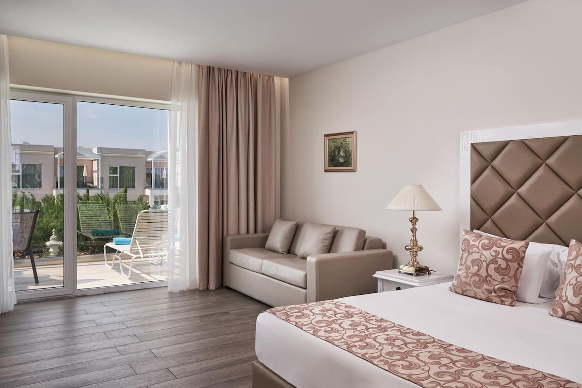 Una habitación de hotel con cama, sofá, mesita de noche y vistas al exterior.