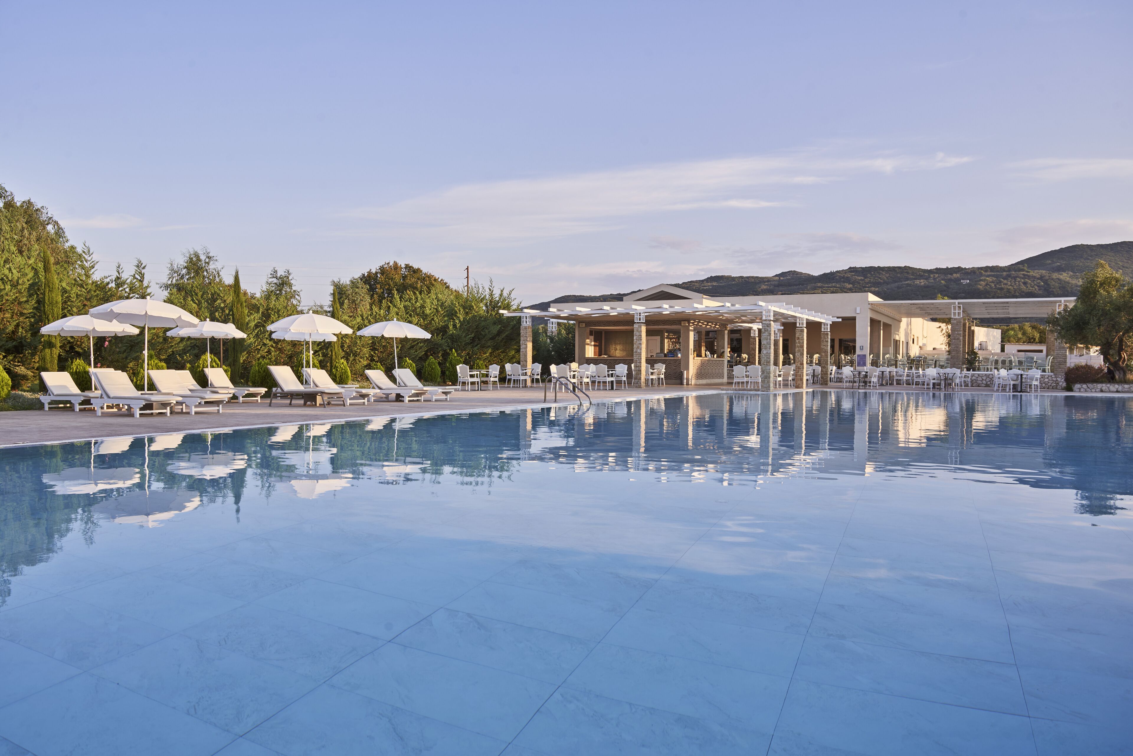A pool area with lounge chairs and umbrellas, a covered seating area, and a view of hills in the background.