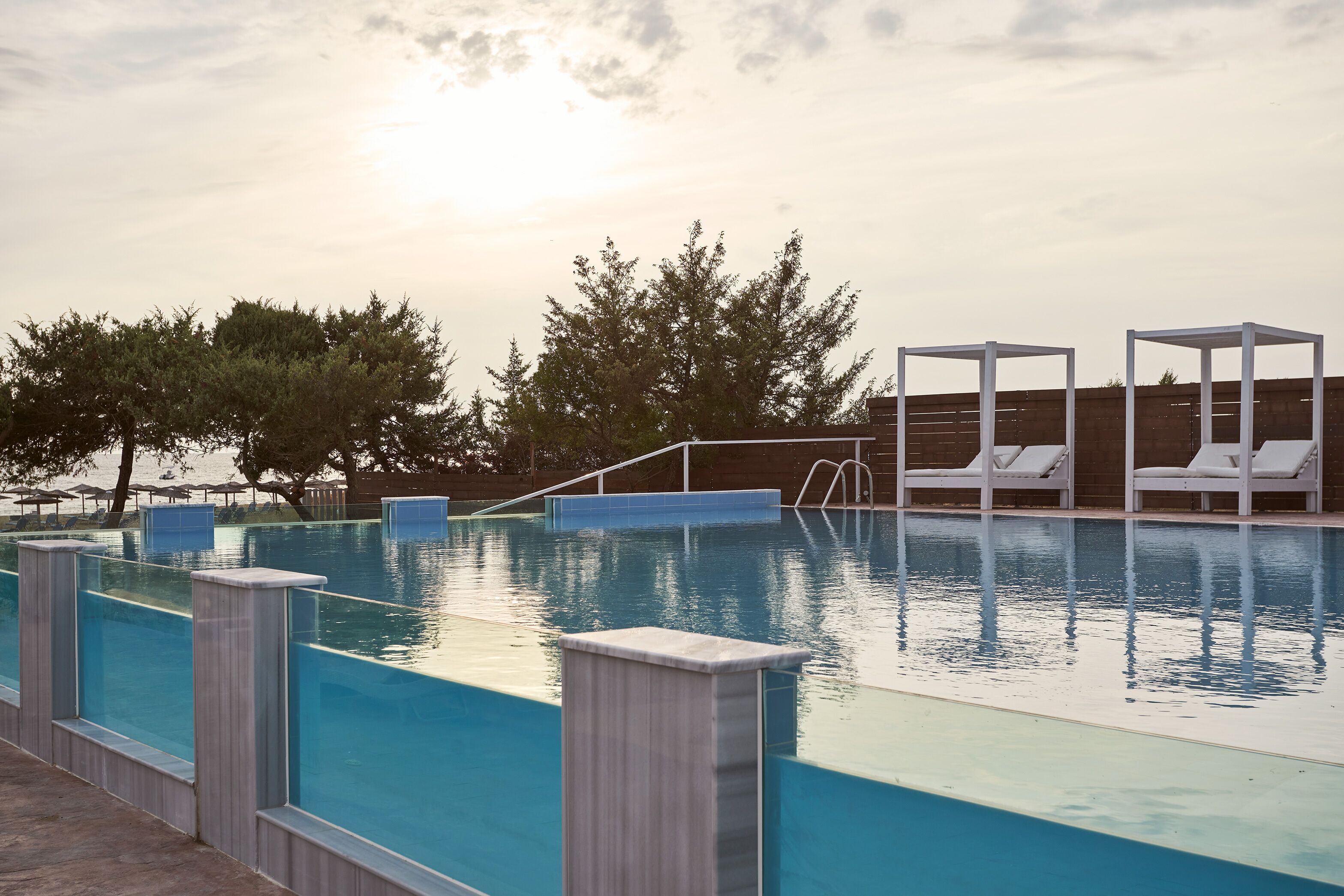 A swimming pool with clear blue water, surrounded by white lounge chairs and a wooden deck.