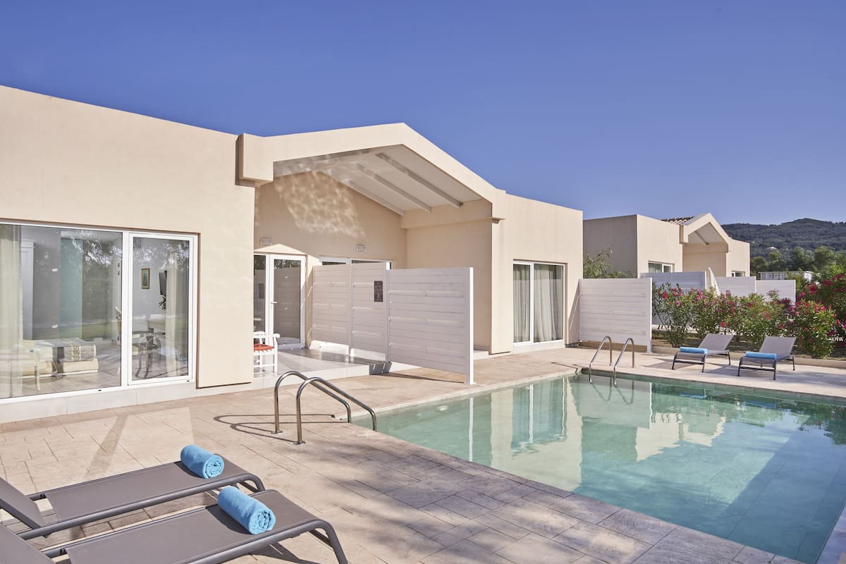 Un área de piscina con sillones de descanso y una sala con paredes de vidrio.