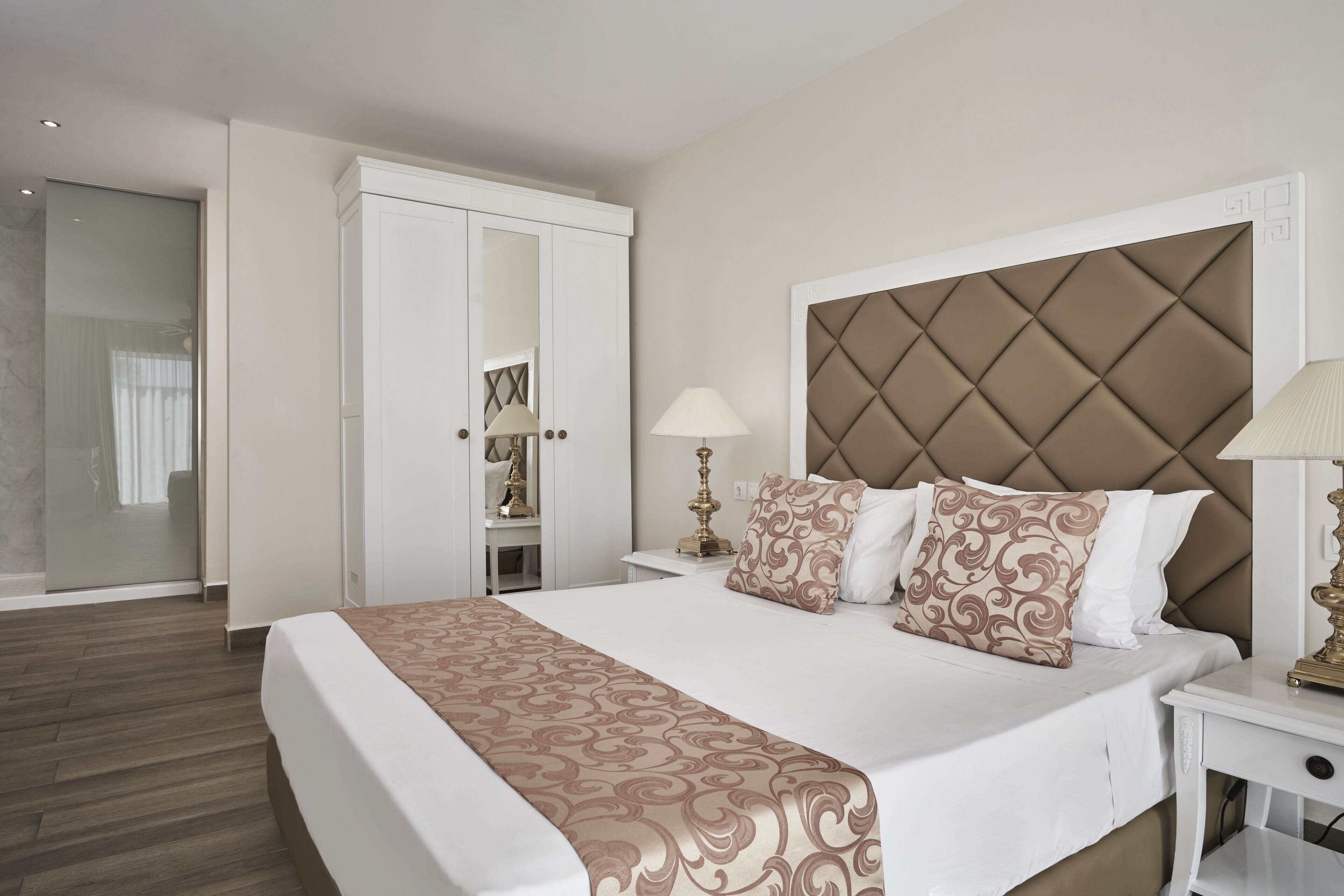 A hotel room with a large bed, a wardrobe, a bedside table with a lamp, and a mirror.