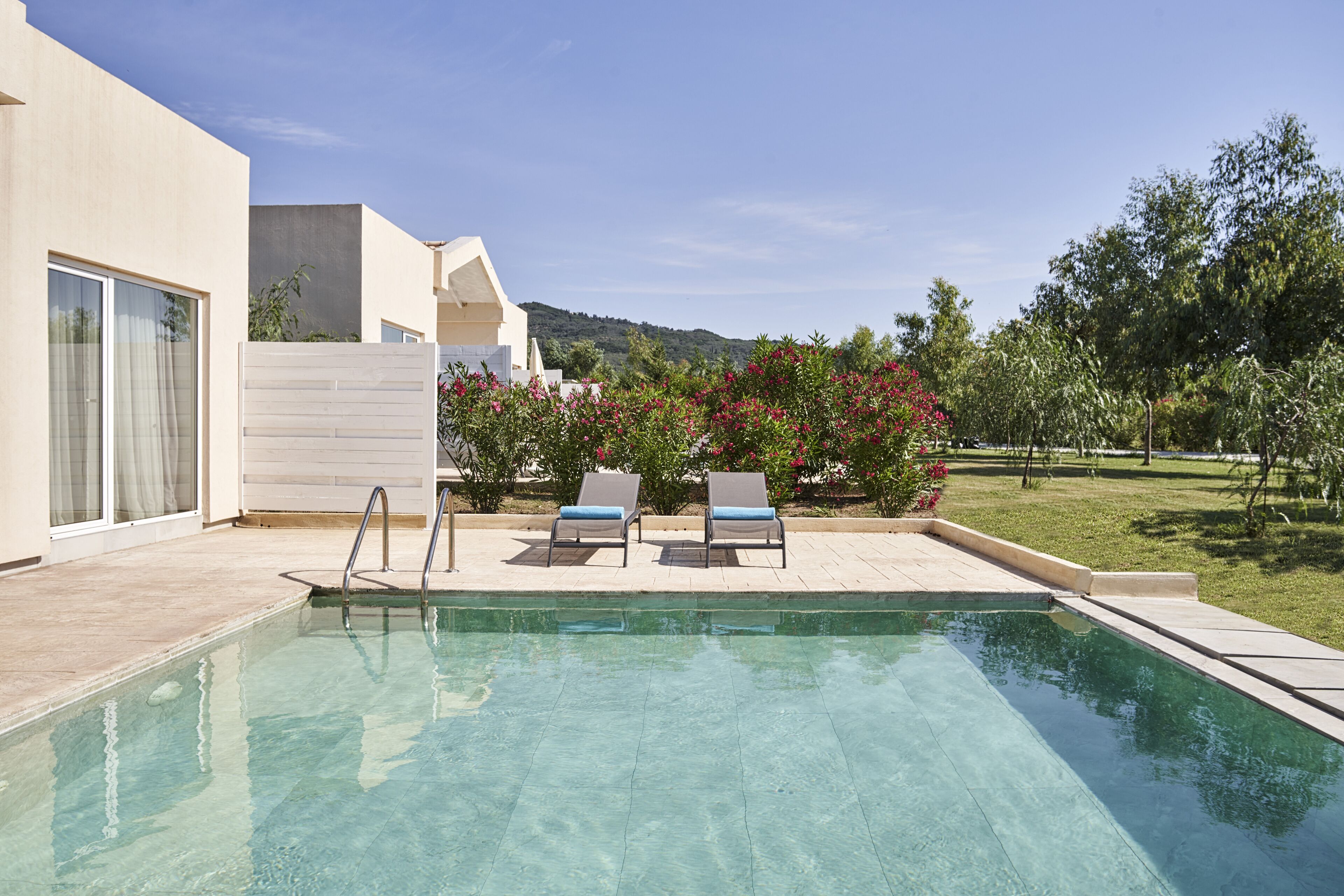 A swimming pool with two lounge chairs, a wooden fence, and a view of a hilly landscape.