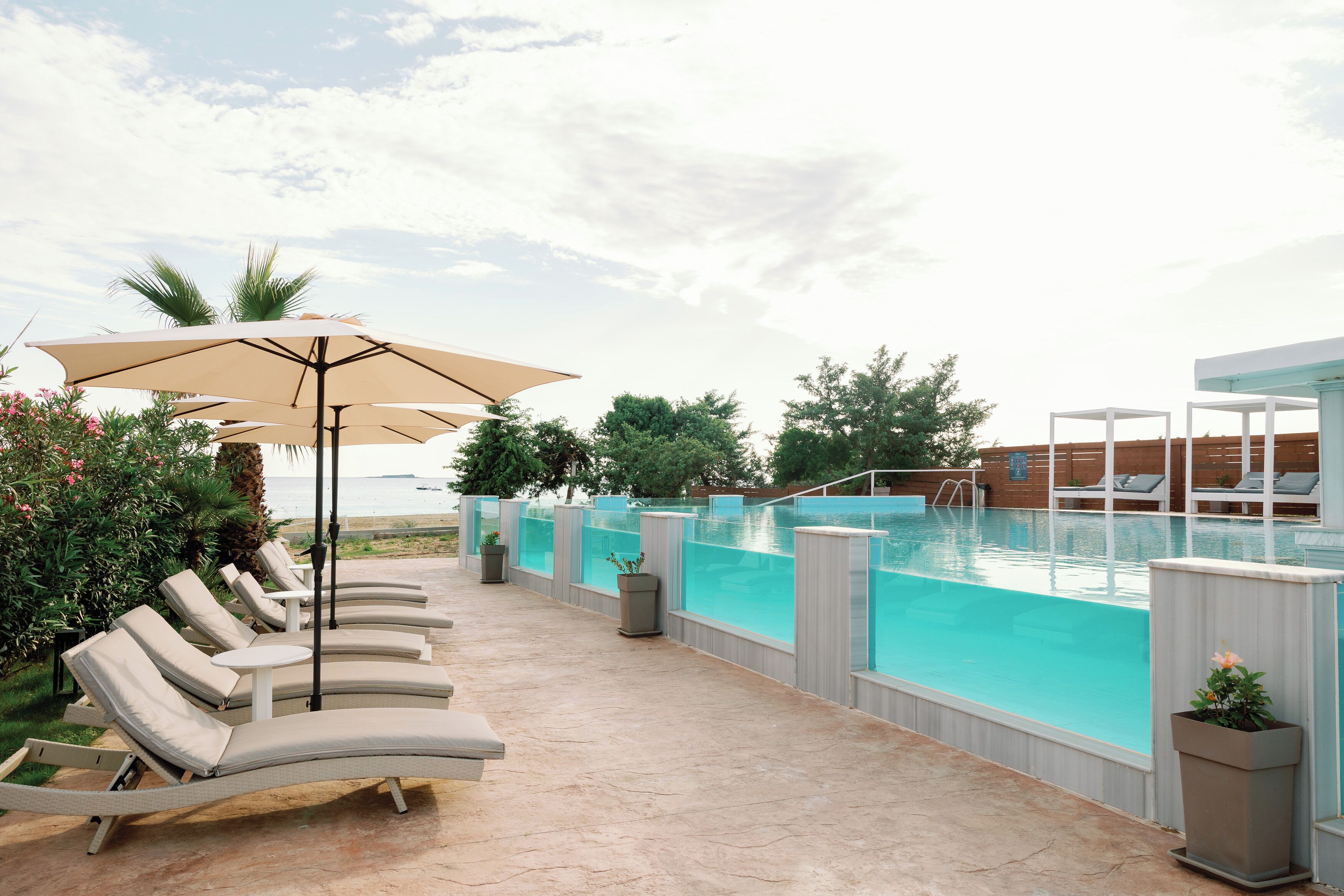 A poolside area with lounge chairs and umbrellas, a pool with a wooden deck, and a view of the ocean.