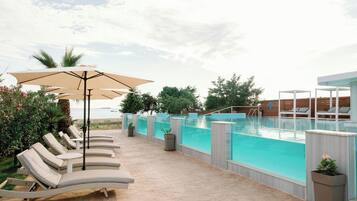 A poolside area with lounge chairs and umbrellas, a pool with a wooden deck, and a view of the ocean.