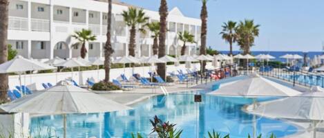 A poolside dining area with a clear view of the pool, palm trees, and a hotel building in the background.