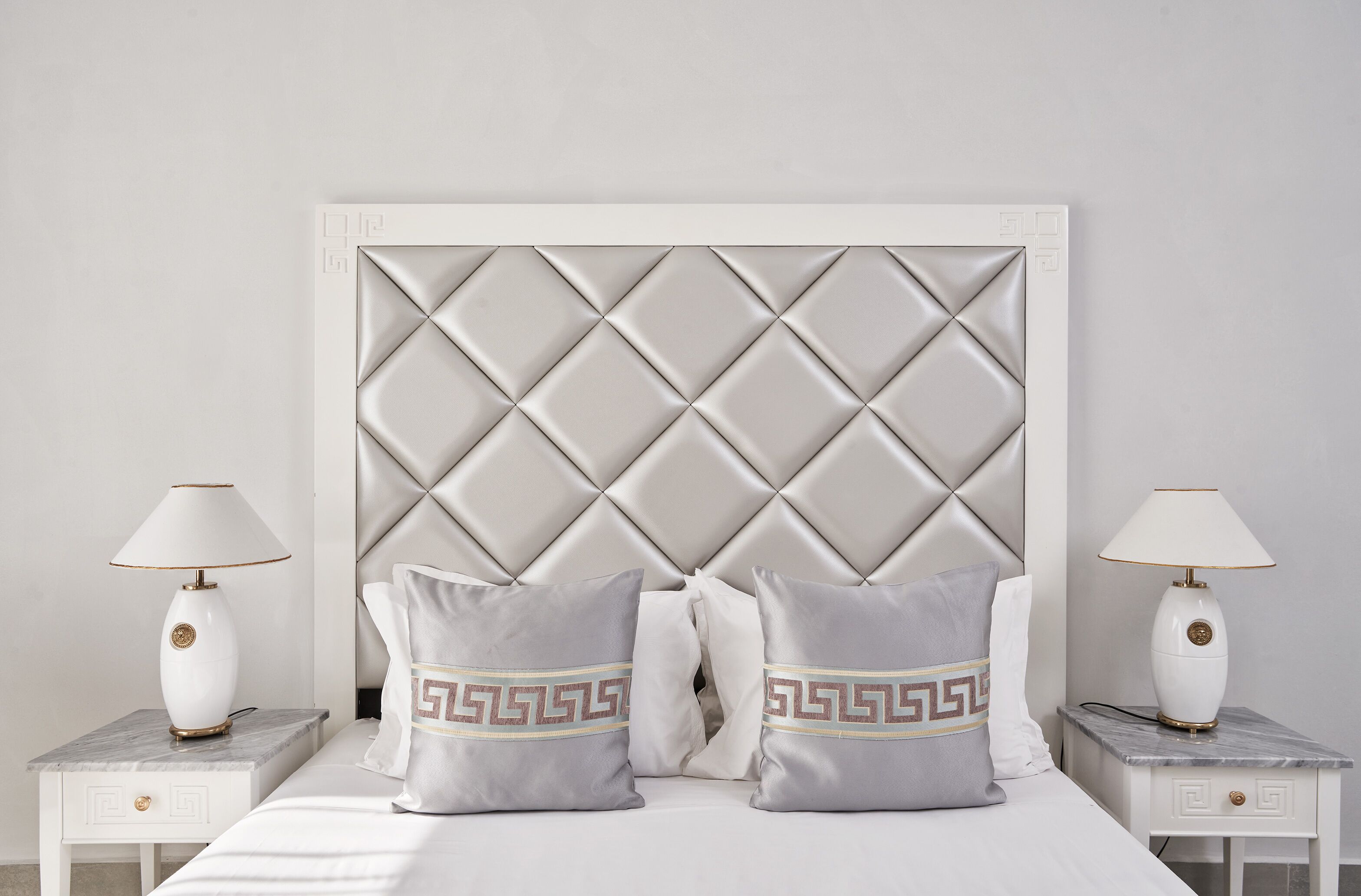 A bedroom with a tufted headboard, two bedside tables with lamps, and two pillows with a geometric pattern.