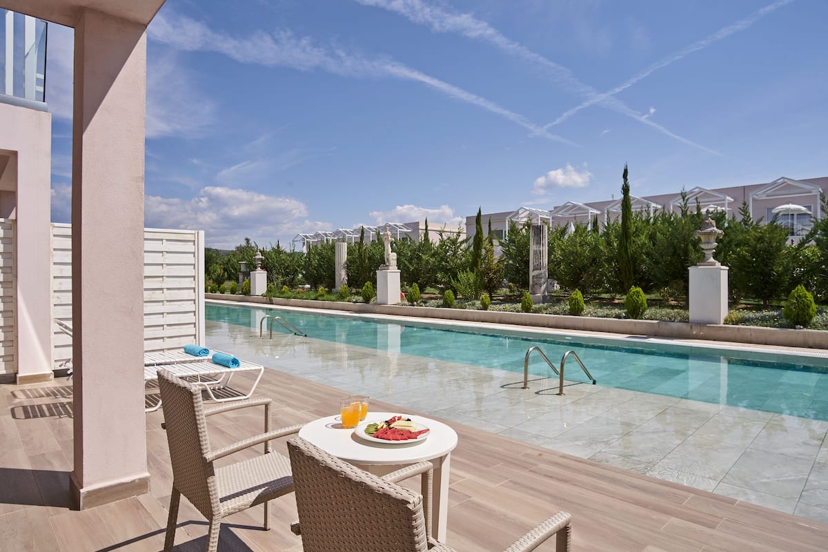 Un área junto a la piscina con una mesa para dos, una estatua y vistas a la piscina y edificios al fondo.