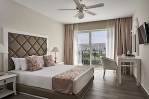 A hotel room with a bed, desk, chair, ceiling fan, and a view of the outside.