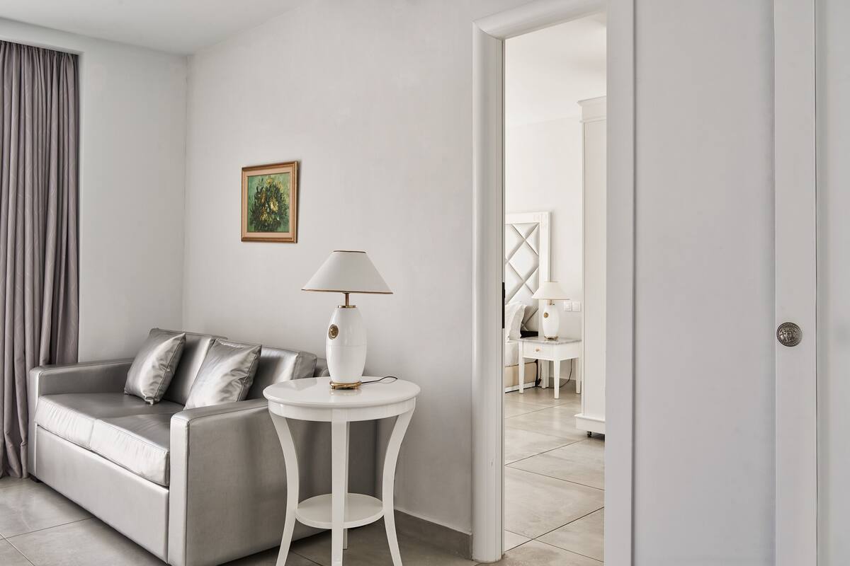 Una sala de estar moderna y minimalista con un sofá gris, una mesita de noche blanca y una lámpara.