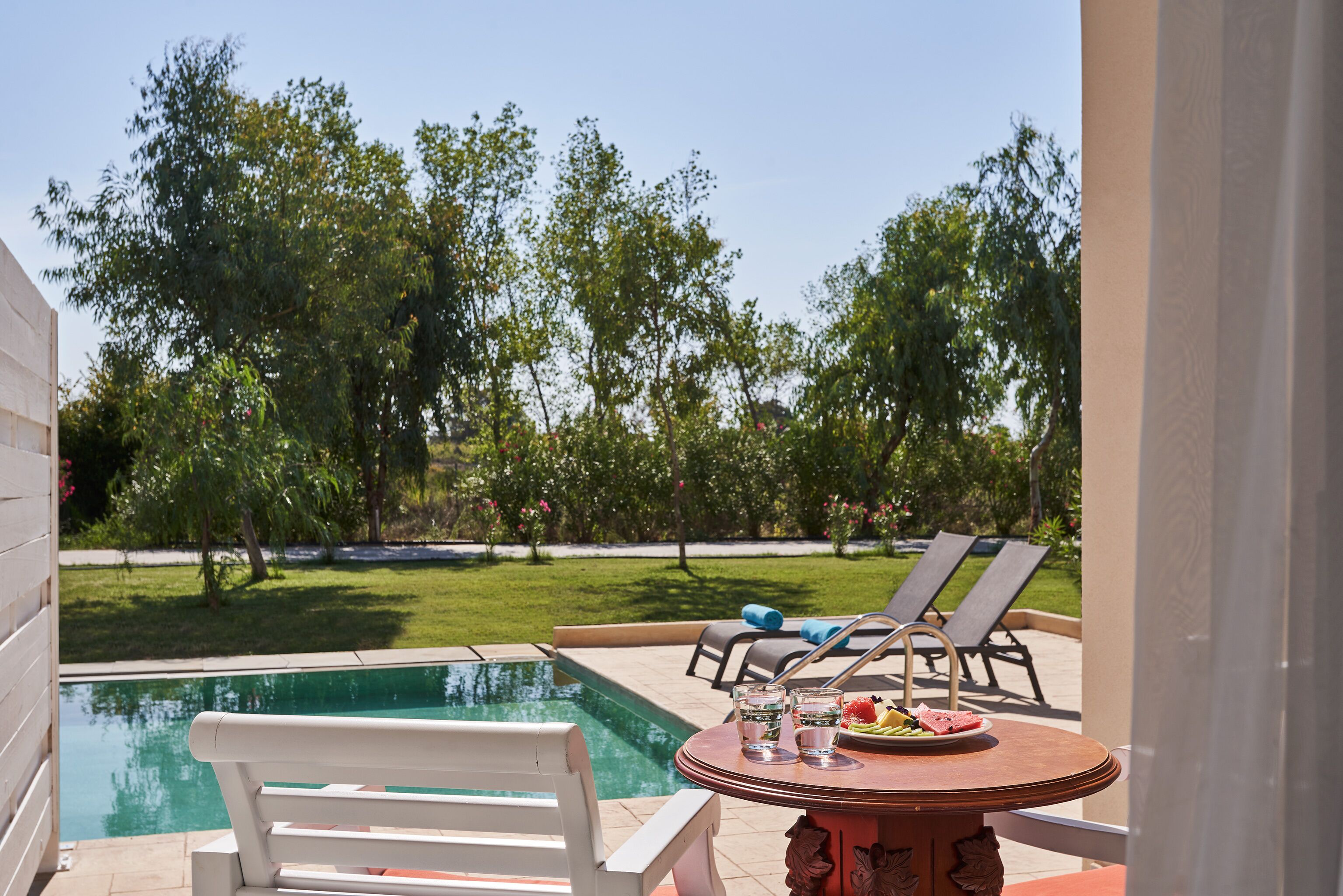 A poolside area with a table, chairs, and a view of the pool and greenery.
