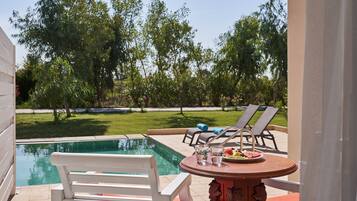 A poolside area with a table, chairs, and a view of the pool and greenery.