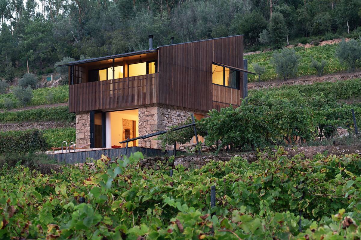 A modern two-story house with a stone foundation and wooden exterior, surrounded by a vineyard.