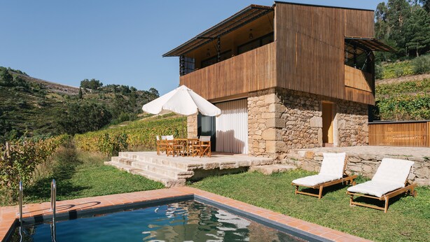 A modern house with a stone foundation, a wooden deck, a swimming pool, and a patio with lounge chairs. - Quinta de Recião (Lamego)