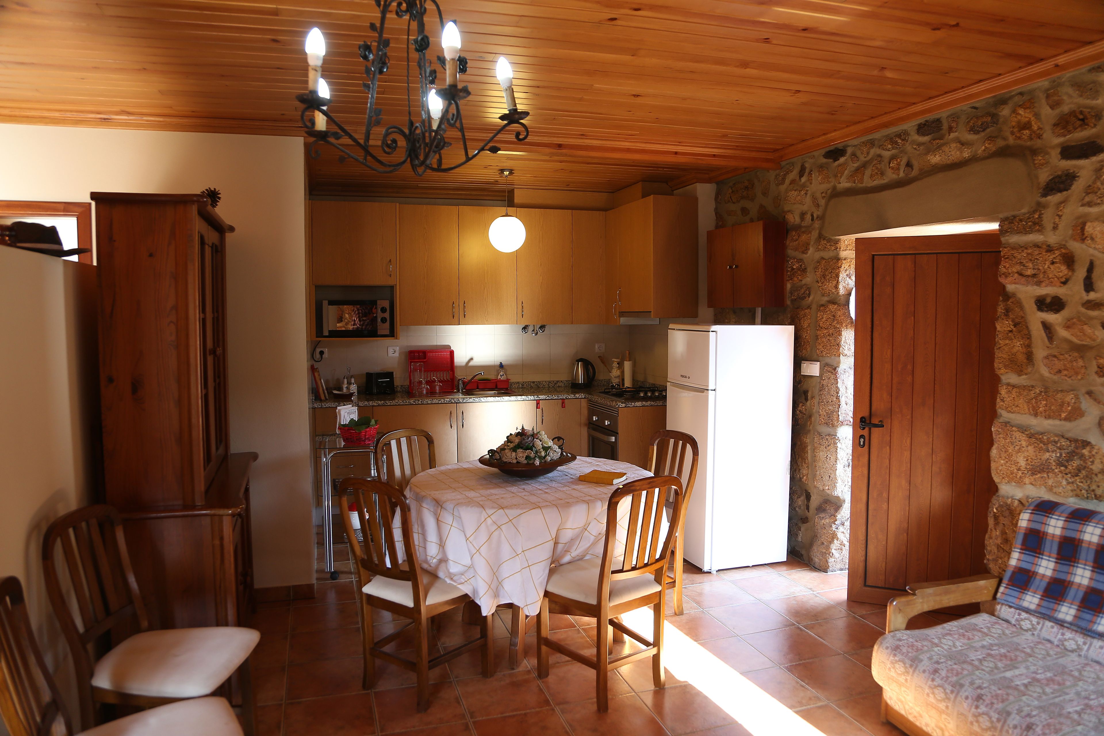 A cozy kitchen with wooden cabinets, a dining table with chairs, and a stone wall.