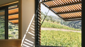 A bedroom with a large window overlooking a vineyard, a bed with white linens, and a wooden ceiling structure. - Quinta de Recião (Lamego)