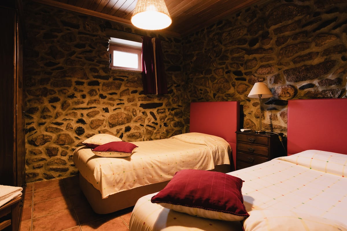 A bedroom with two beds, stone walls, a wooden ceiling, and a window.